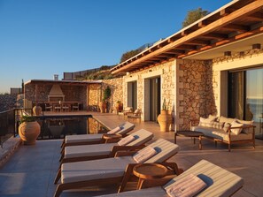 Eine Dachterrasse mit Liegestühlen, einem Pool und einem Steinhaus mit großen Fenstern.