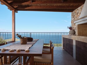 Ein Holztisch mit Stühlen und einer gewebten Matte, mit Blick auf die Küste.