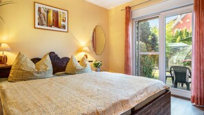 Un dormitorio con una cama grande, dos lámparas de noche, un cuadro en la pared y un ventanal corredero que da a un espacio exterior.