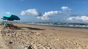 A beach with a clear sky, waves, and a blue umbrella.