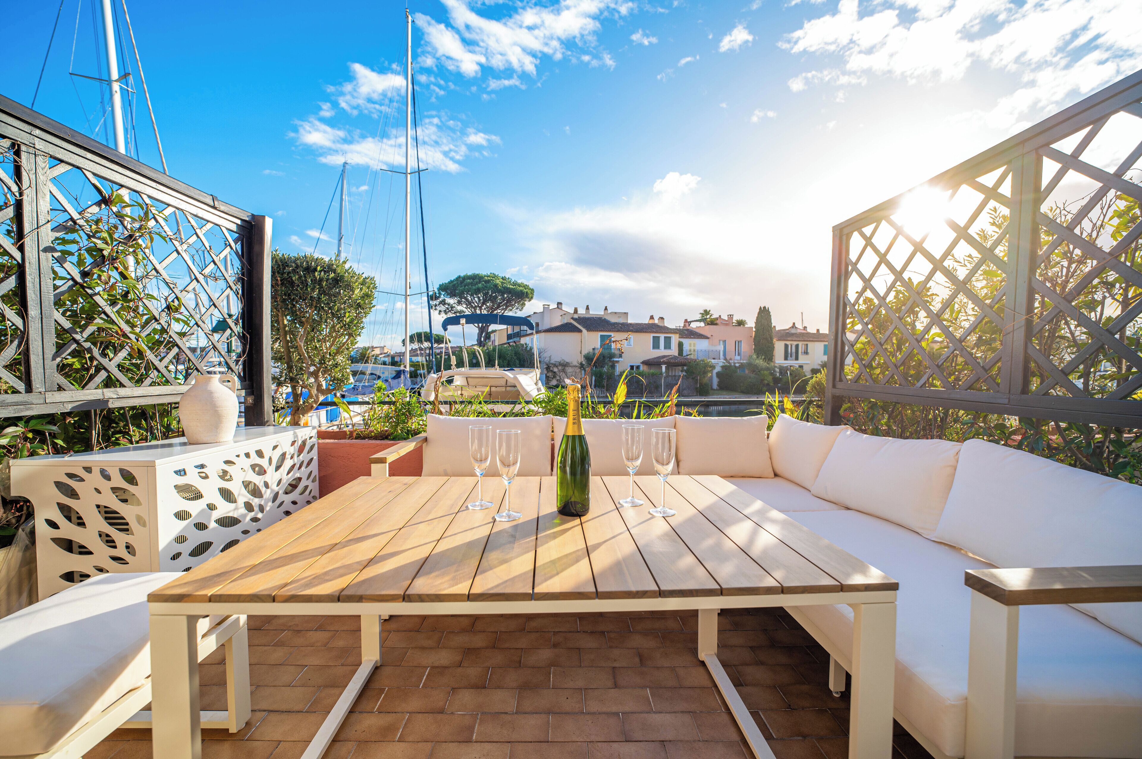 A patio with a wooden table, white sofa, and a bottle of champagne.