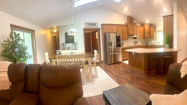 Un amplio salón con una mesa de comedor y sillas, una cocina con armarios de madera y un refrigerador de acero inoxidable, y una zona de estar acogedora con un sofá y una mesita.