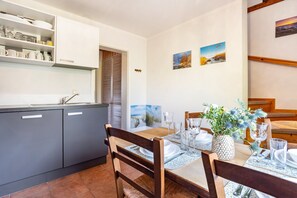 Ein Essbereich mit Holztisch, gedeckt für vier Personen, eine Küche mit grauen Schränken und zwei gerahmte Bilder an der Wand.