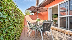Eine Terrasse im Freien mit Tisch und Stühlen, einem Blumentopf und einem großen Fenster.