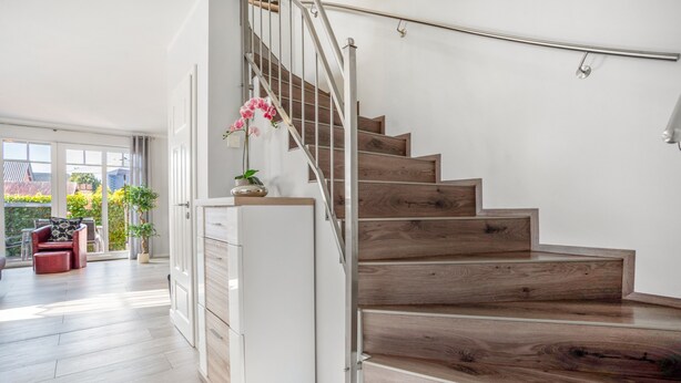 Eine Treppe mit Holzstufen und einem Metallgeländer, die zu einer Empore mit einem weißen Schrank und einem Blumentopf führt.