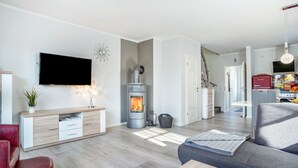 Ein modernes Wohnzimmer mit Kamin, Flachbildfernseher, Sofa und Essbereich.