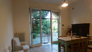 Comedor con una mesa preparada para cuatro personas, una silla, un radiador y vistas a un jardín exterior a través de un ventanal.