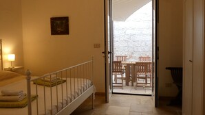 Una habitación de hotel con una cama, una mesita de noche, una lámpara y una puerta que da a un patio exterior con muebles de madera.