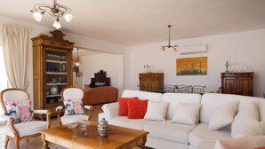 Ein Wohnzimmer mit einem weißen Sofa, einem Holztisch und zwei Stühlen mit floralen Kissen.