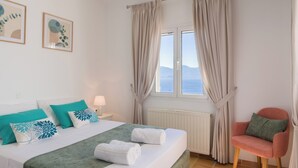 Ein Hotelzimmer mit Bett, Stuhl, Fenster mit Vorhängen und einem Bild an der Wand.