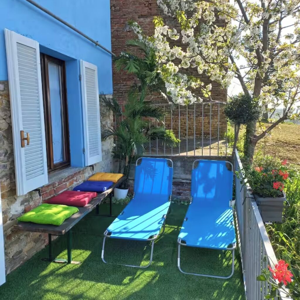 Une terrasse avec deux fauteuils de jardin bleus, une petite table avec des coussins et un mur de briques agrémenté de volets.