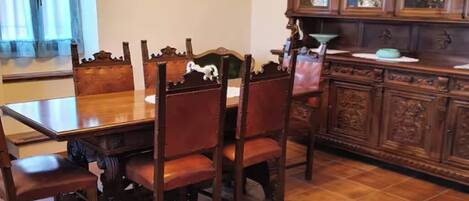 Un comedor con mesa y sillas de madera, un sofá verde y un aparador con puertas de vidrio.