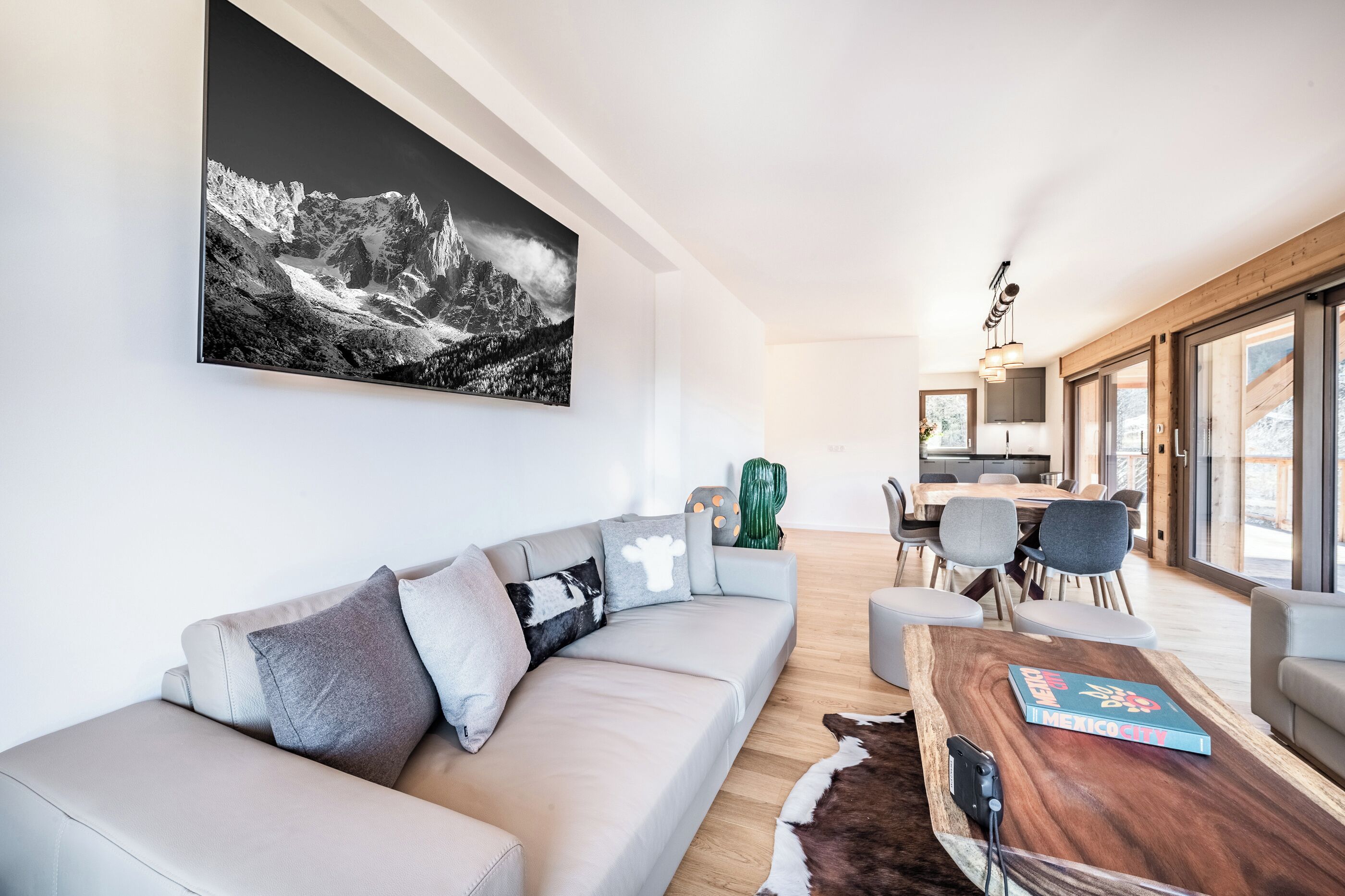A modern living room with a sofa, a wooden coffee table, and a large black and white mountain painting.