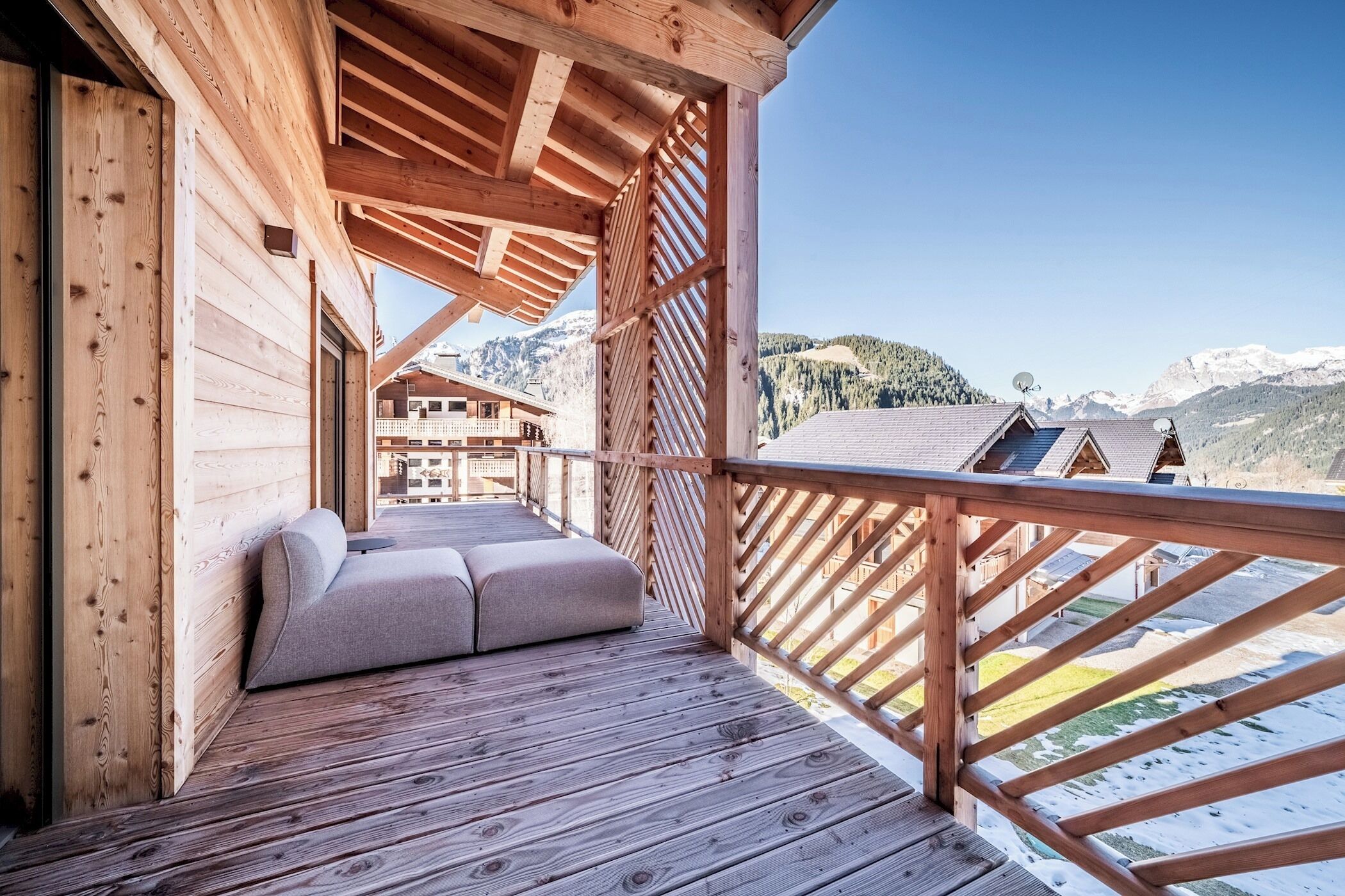 Un terrazzo in legno con un divano e dei cuscini, affacciato su un paesaggio montuoso.