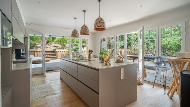 A modern kitchen with a central island, pendant lights, and large windows offering a view of the outdoors. - L'écrin du Ferret *Swimming pool *Air conditioning *Spa (Lège-Cap-Ferret)