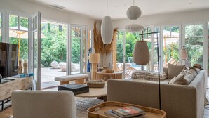 A spacious living room with large windows, a sofa, a coffee table, and a TV. - L'écrin du Ferret *Swimming pool *Air conditioning *Spa (Lège-Cap-Ferret)