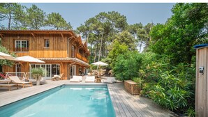 A wooden cabin with a pool, outdoor seating, and lush greenery. - L'écrin du Ferret *Swimming pool *Air conditioning *Spa (Lège-Cap-Ferret)