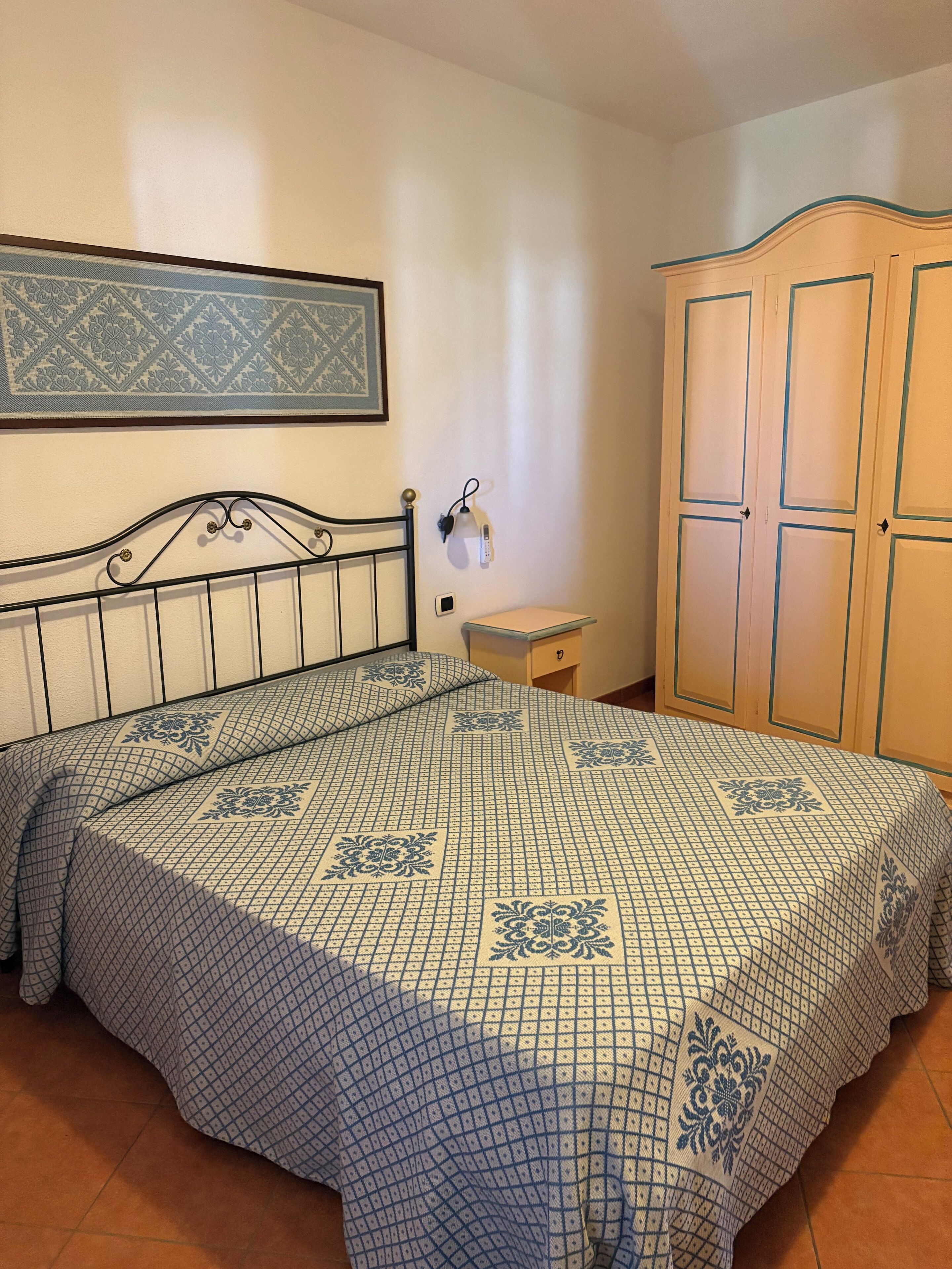 Un dormitori amb un llit, una tauleta de nit, un armari i una làmpada penjada a la paret.