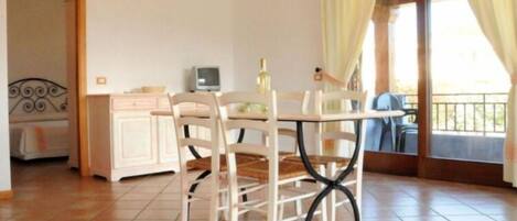 Una habitación con una mesa de comedor, sillas, un mueble bajo, un televisor y un balcón con cortinas.