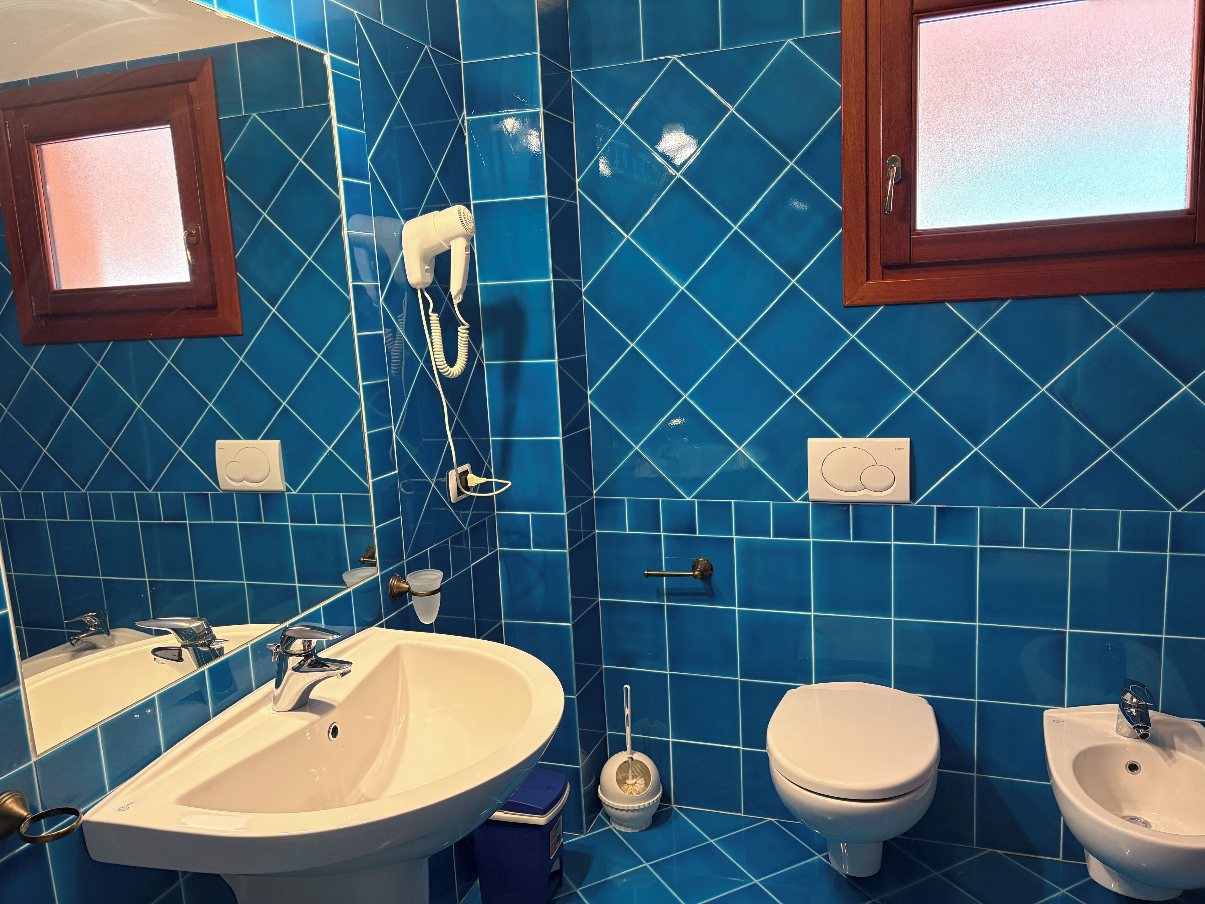 A bathroom with blue tiles, a white sink, a toilet, and a bidet.