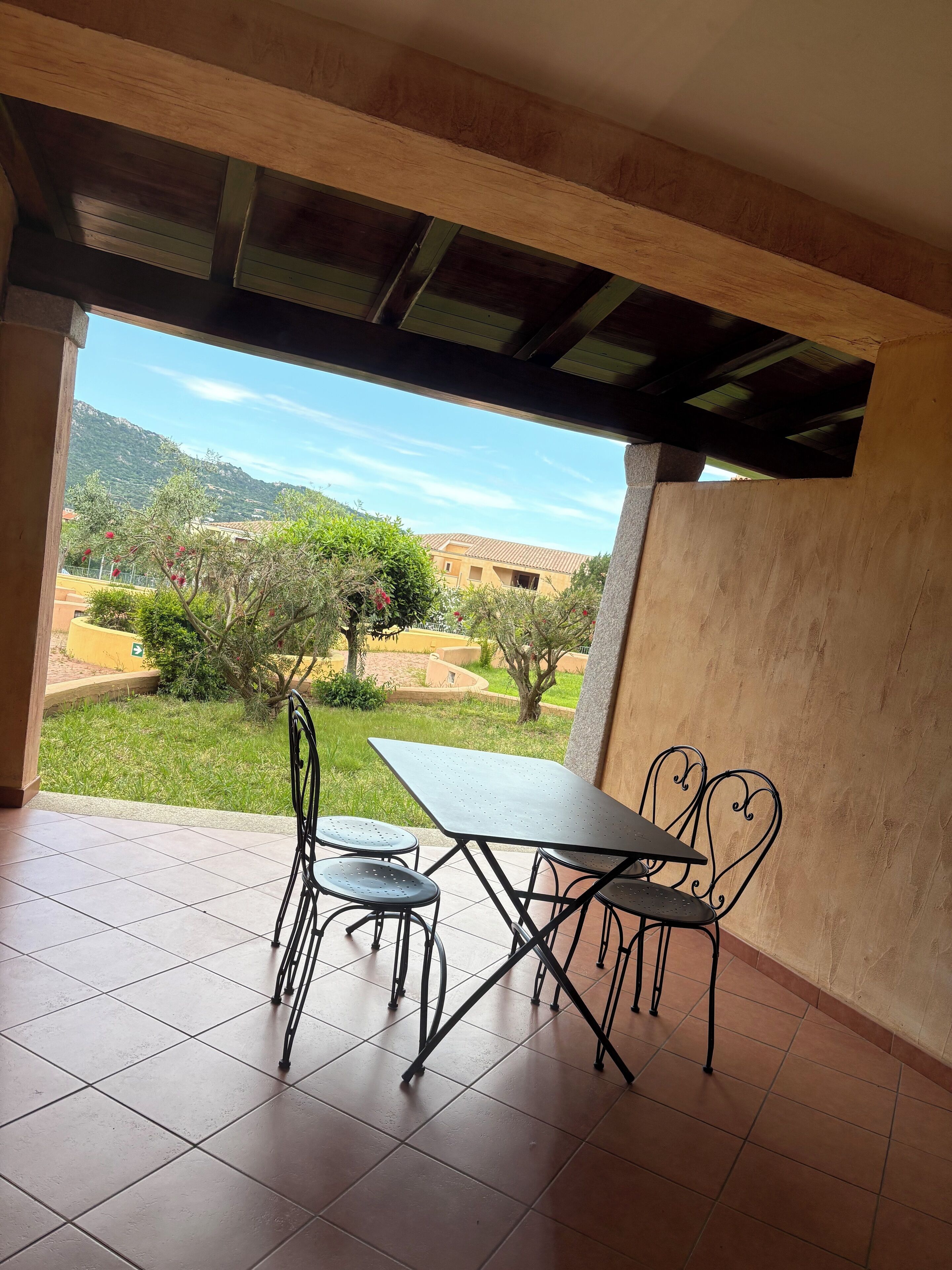 A covered patio with a table and chairs, a tiled floor, and a view of a mountainous landscape.