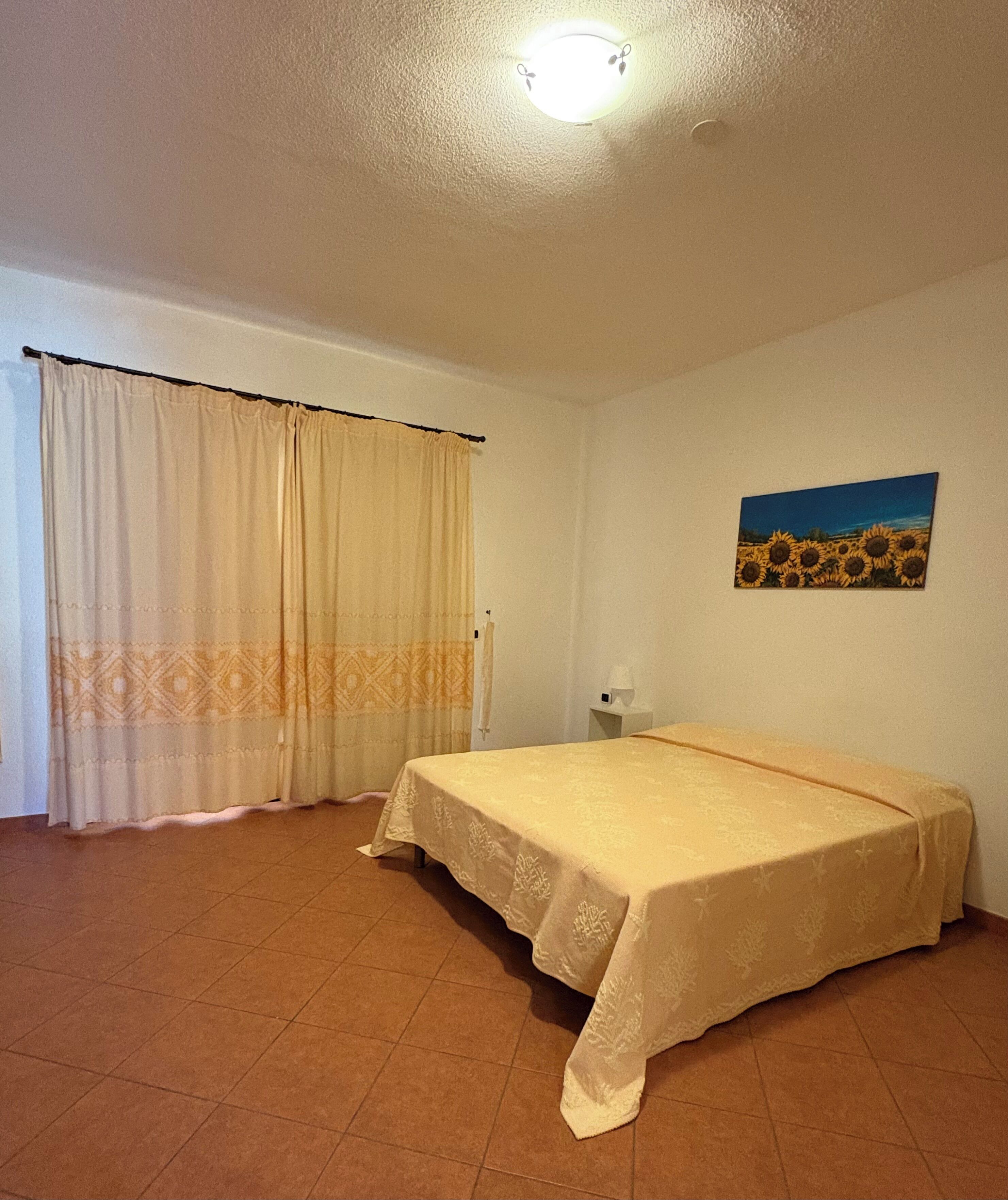 Ein Zimmer mit Bett, Vorhängen, einem Gemälde und einer Deckenleuchte.