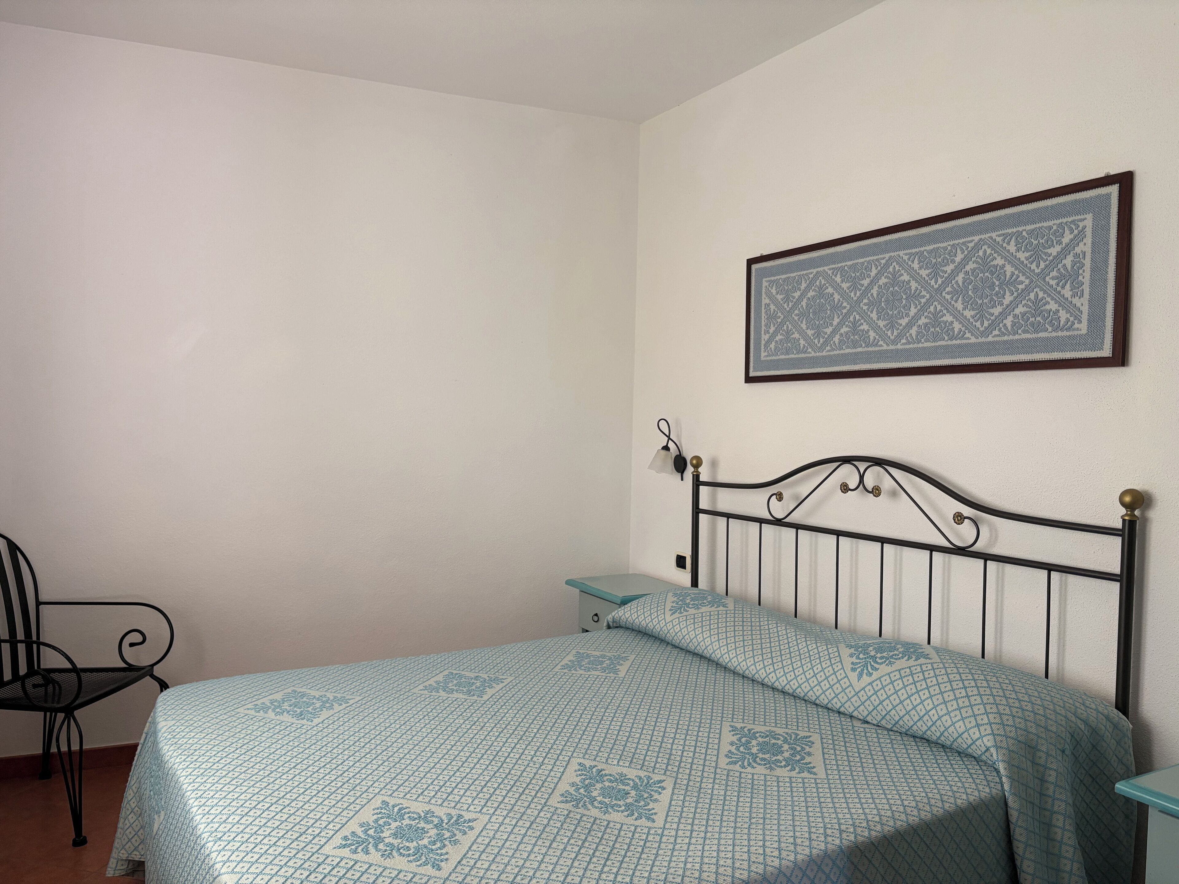 Een slaapkamer met een eenpersoonsbed, een stoel, een nachtkastje en een ingelijst schilderij aan de muur.