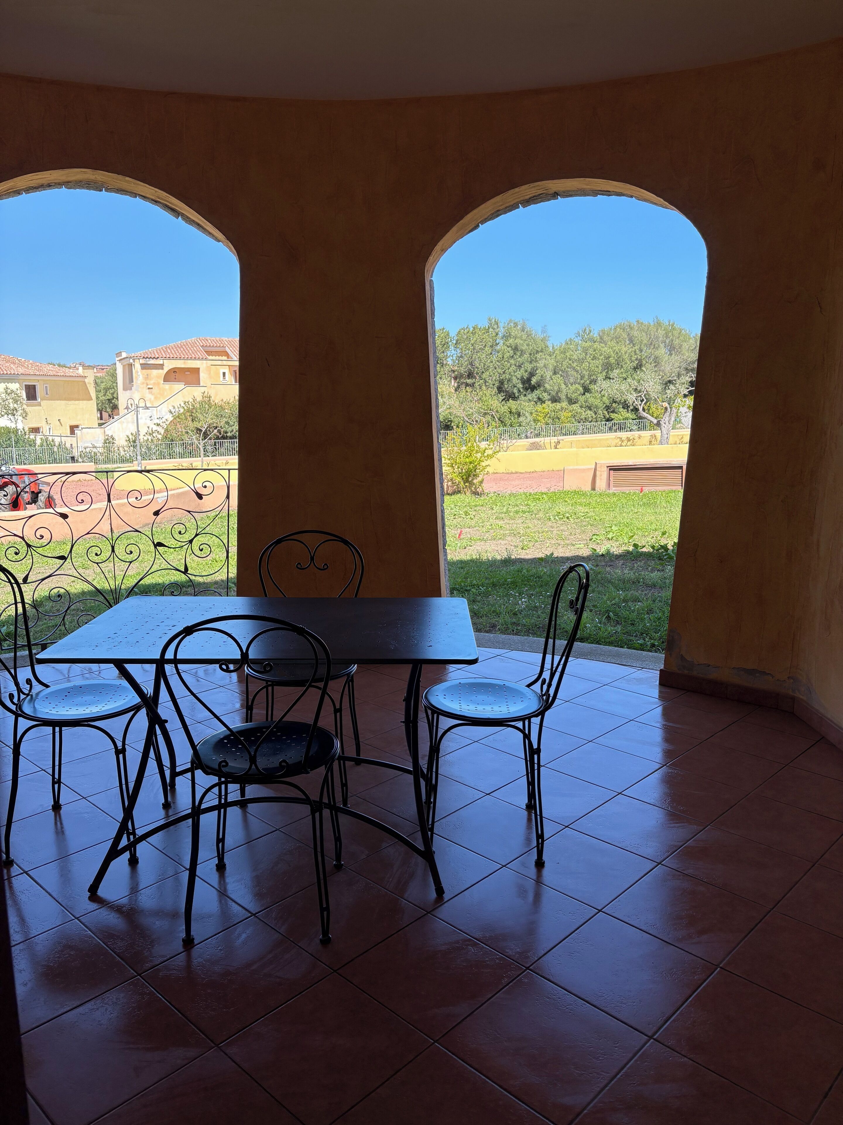 A dining area with a table and four chairs, two large arched windows, and a view of a residential area.