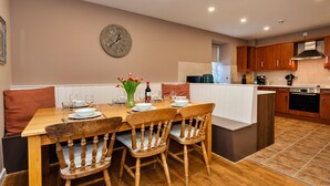 Une cuisine moderne avec des meubles en bois, un coin repas avec une table et des chaises en bois, et une horloge au mur.