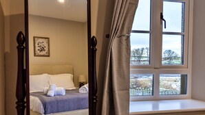Une chambre à coucher avec un lit à baldaquin, une fenêtre donnant sur les arbres et un tableau encadré au mur.