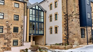 Un immeuble à plusieurs étages, dont l’architecture combine des éléments de style classique en pierre et des éléments modernes, avec de grandes fenêtres et une cour enneigée.