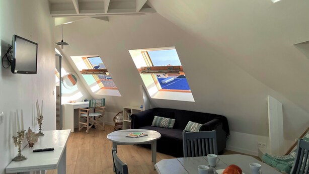 Et moderne loftværelse med spiseplads, sofa og to ovenlys med udsigt over bybilledet.