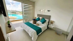 Un dormitorio con cama, mesita de noche, lámpara, vista a una piscina y una planta en maceta.