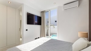 Een moderne slaapkamer met een groot bed, een flatscreen televisie aan de muur en een schuifdeur naar een zwembad.