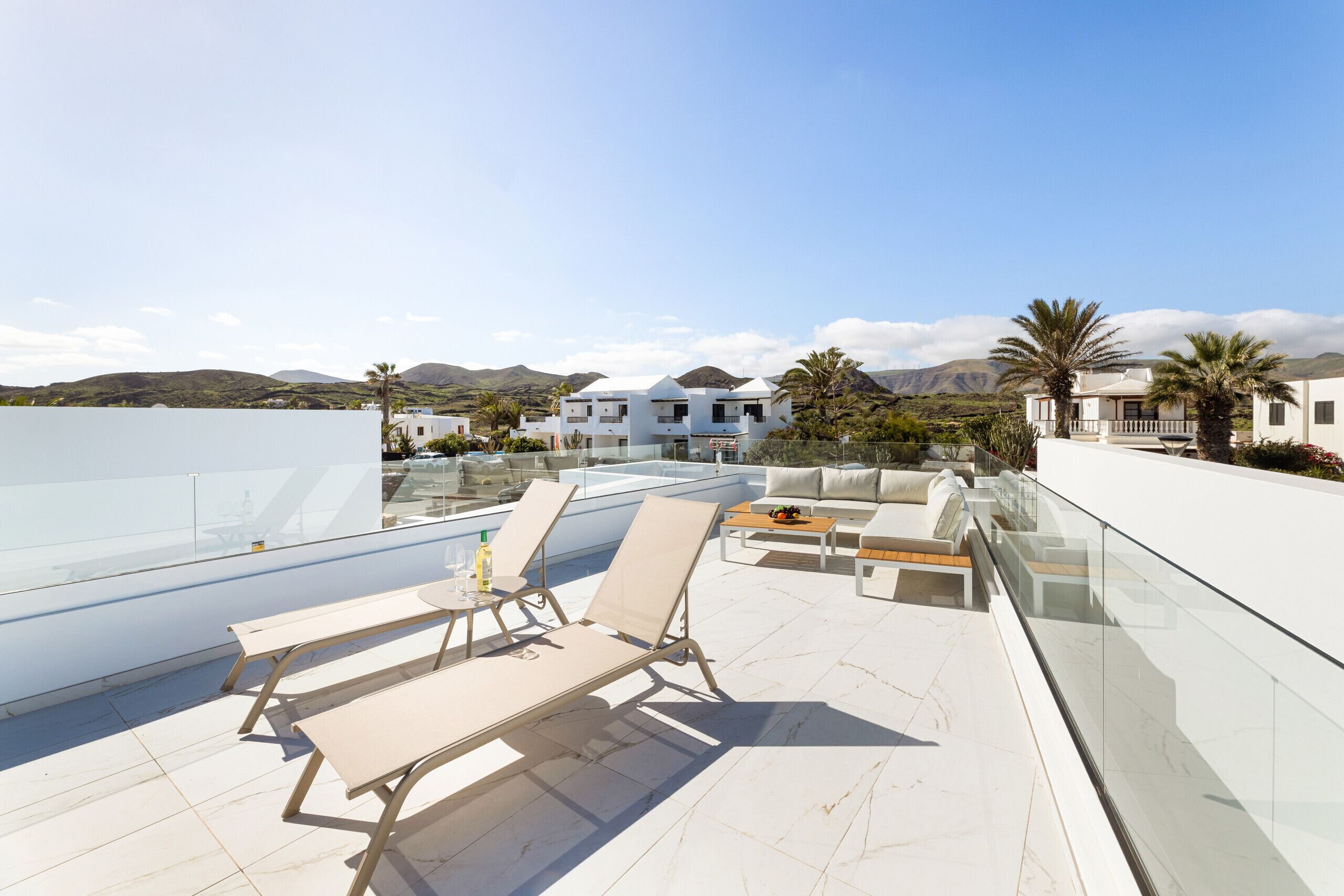 Una terrazza panoramica con poltrone relax, un tavolino e una ringhiera in vetro che si affaccia su un paesaggio montuoso.