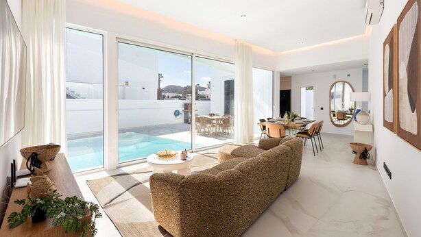 Een moderne woonkamer met een grote bank, een eethoek en uitzicht op een zwembad.