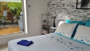 A hotel room with a bed, a window, a small shelf with books, and a wall with a mosaic pattern. - Cosy getaway between forest and ocean - swimming pool, jacuzzi & beach on foot (Saint-Pierre)