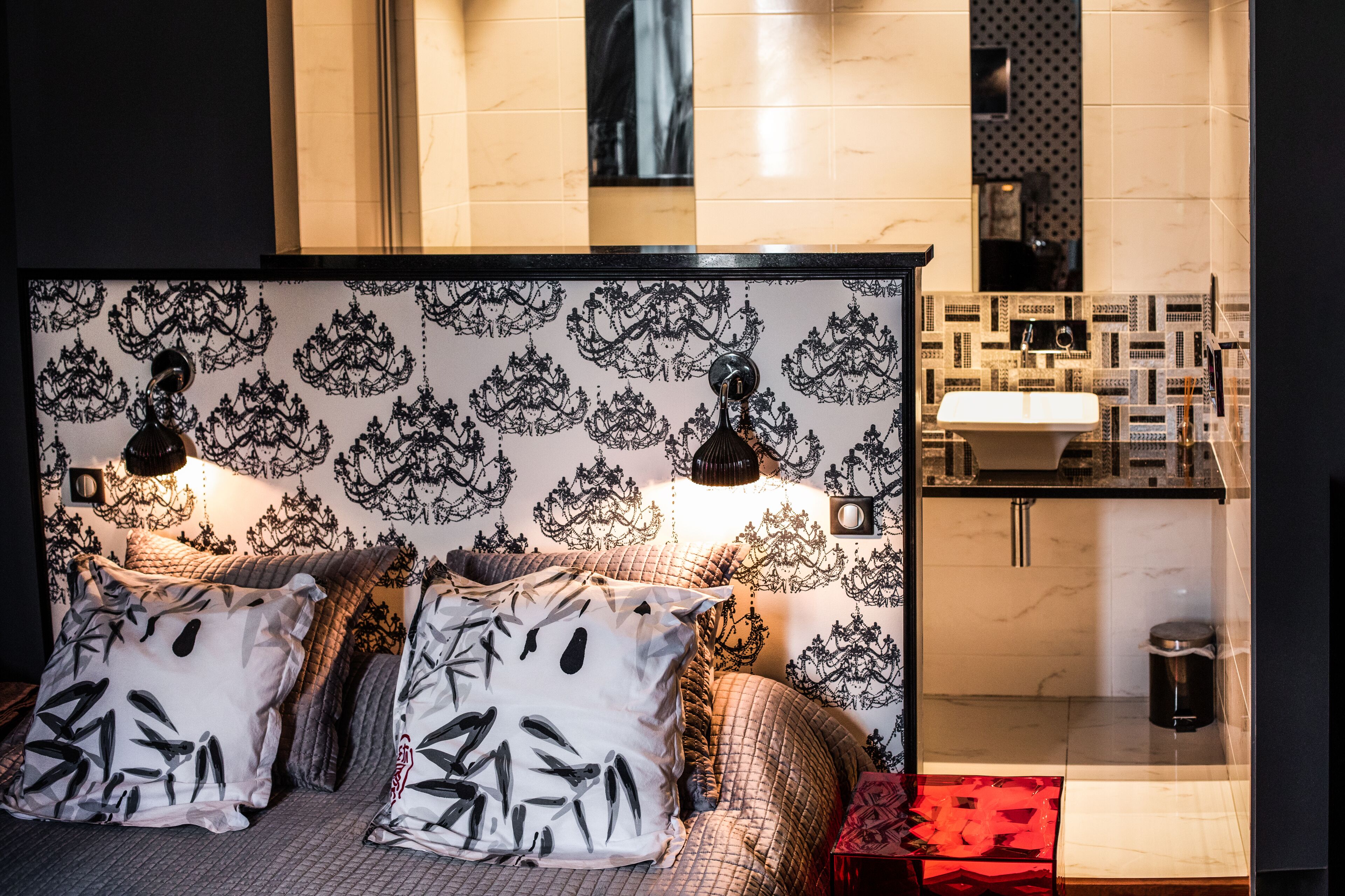 Una habitación de hotel con una cama grande, papel tapiz estampado y un baño moderno con lavabo y espejo.