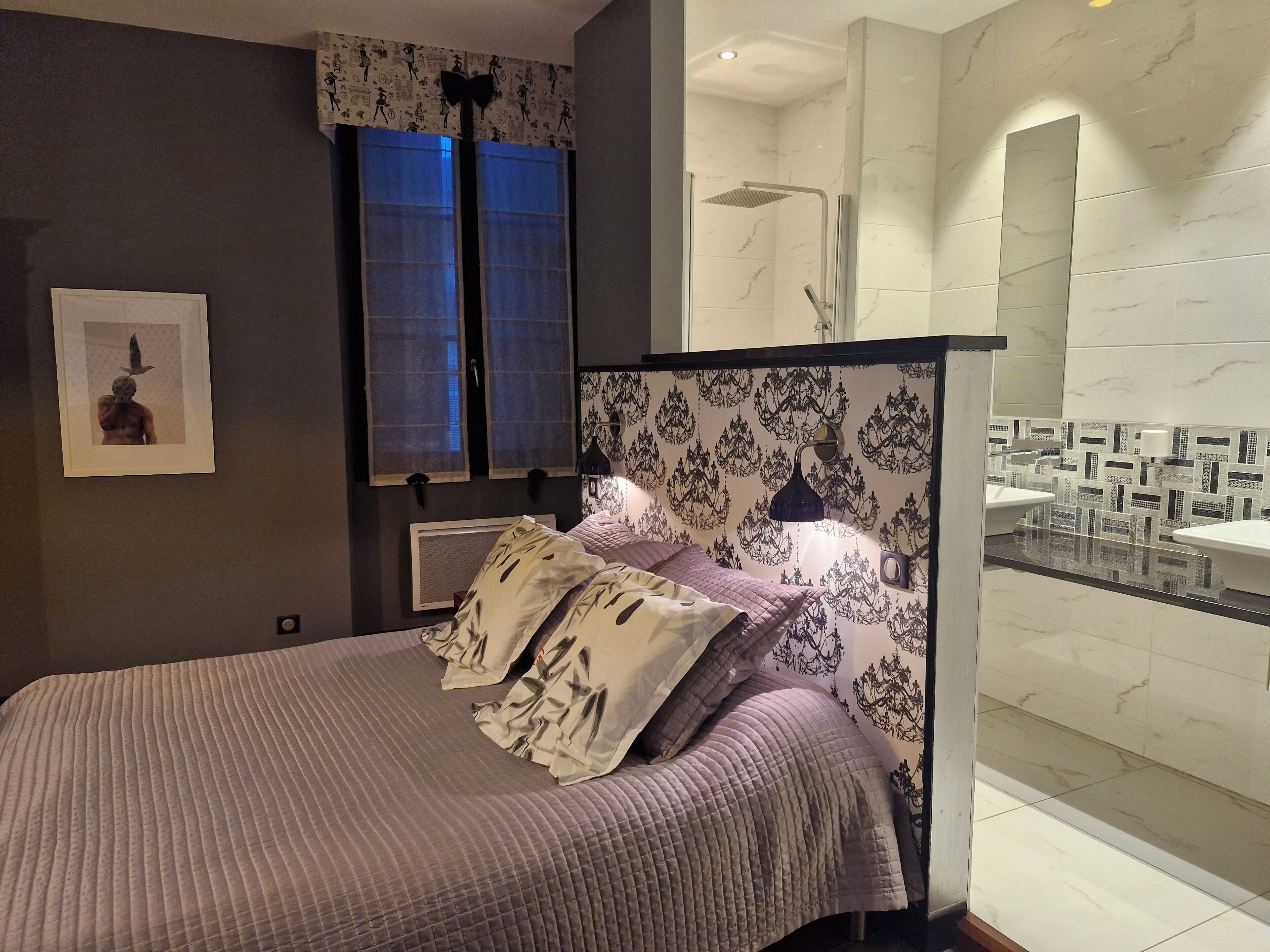 A modern bedroom with a bed, a large mirror, and a bathroom with a sink and shower.