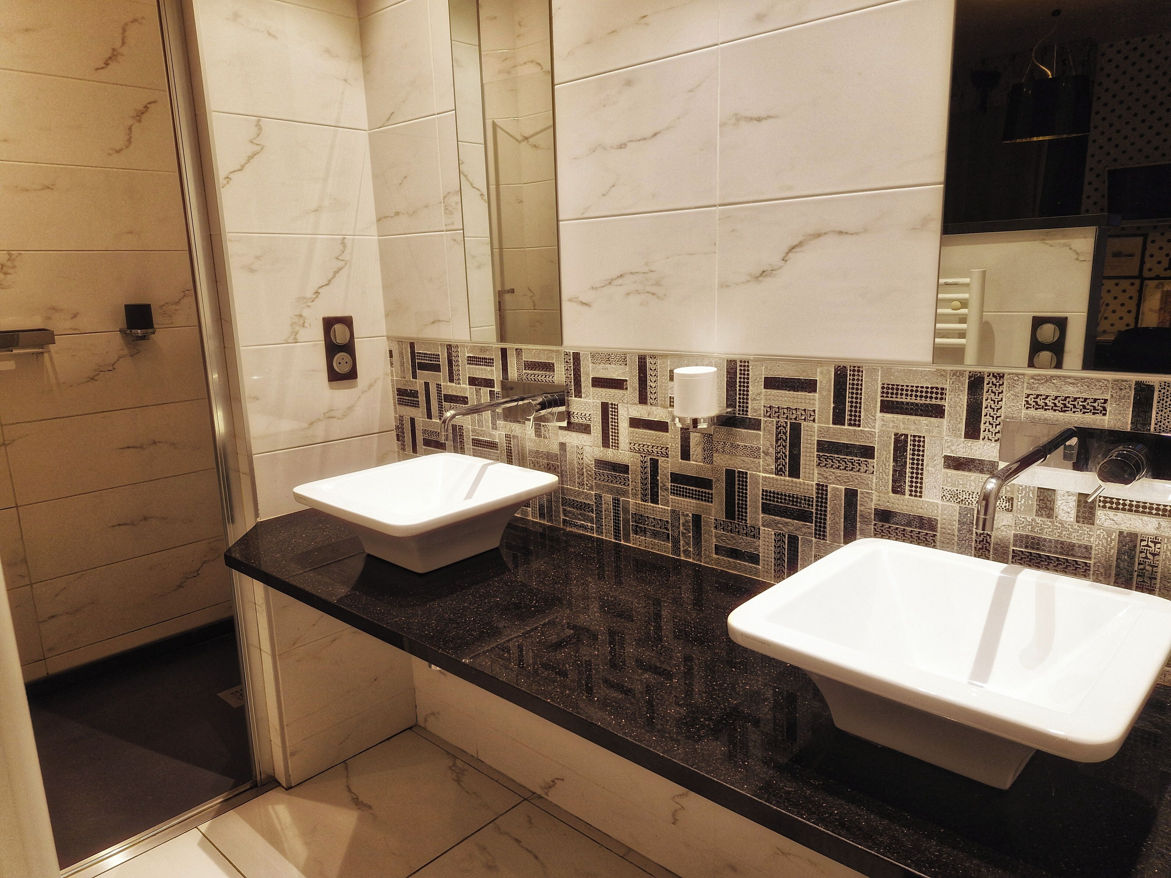 Une salle de bain moderne avec deux lavabos, un miroir et un mur recouvert de carreaux.