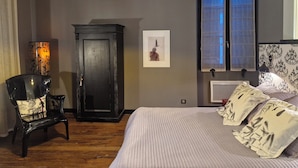 A bedroom with a bed, a chair, a cabinet, a window, and a wall-mounted light fixture. - Onigourmand (Oloron-Sainte-Marie)