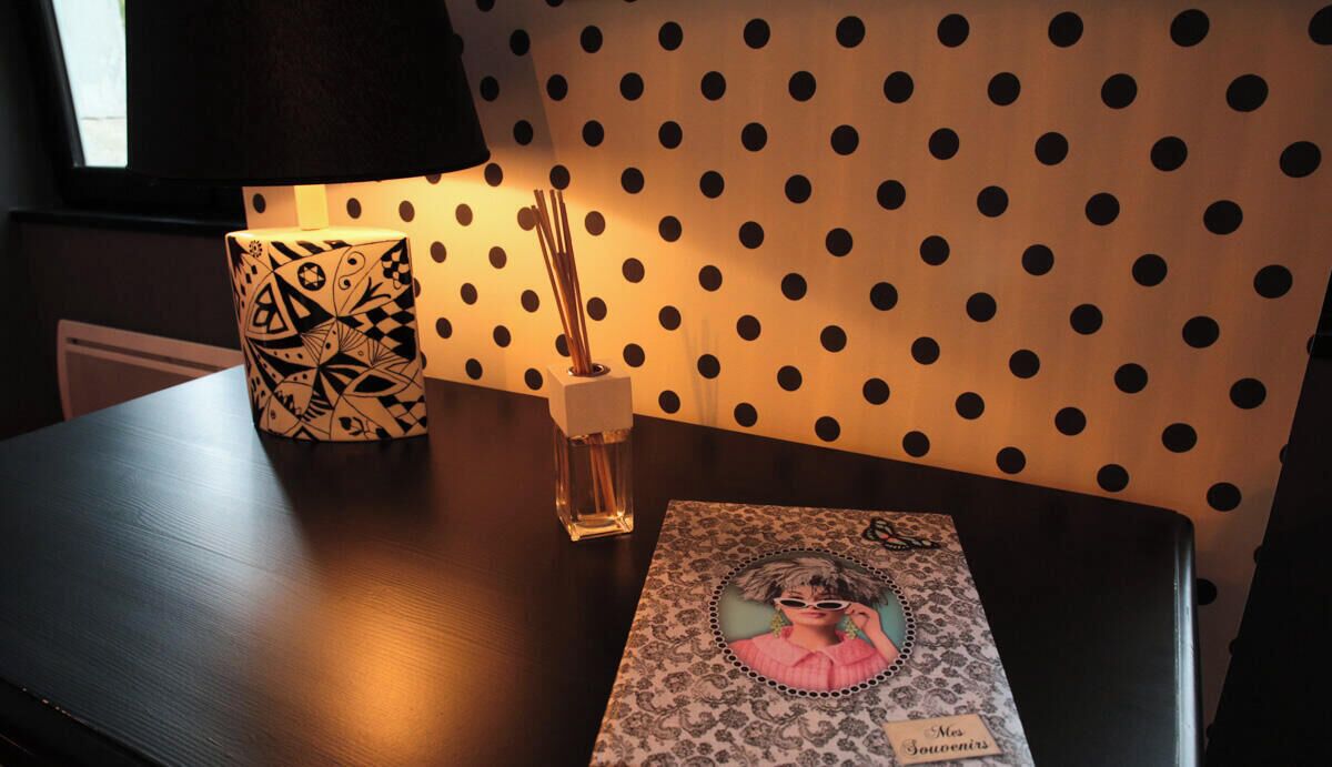A table with a patterned lamp, a photo frame, and a small vase with sticks.