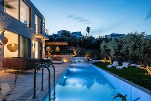 A modern outdoor pool area with a lounge chair, a small table, and a seating area with a glass wall. - Brand New Villa, Private Heated Pool, Quiet,Luxury (Daratsos)