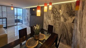 Zona pranzo moderna con parete in marmo, tavolo in vetro e lampadario a sospensione.