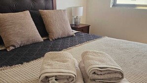 Un letto rifatto con coperte trapuntate, due cuscini e un asciugamano beige ripiegato.