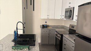 A modern kitchen with white cabinets, a granite countertop, a built-in microwave, and a stainless steel refrigerator. - Cozy Modern Retreat, Peaceful Stay Near Everything (Portsmouth)