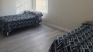 A bedroom with two beds, a ceiling fan, a window with blinds, and a colorful painting on the wall. - Cozy Modern Retreat, Peaceful Stay Near Everything (Portsmouth)