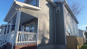 A two-story house with a front porch, a wooden fence, and a clear blue sky. - Cozy Modern Retreat, Peaceful Stay Near Everything (Portsmouth)