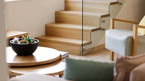 Et moderne interiør med en trappe i træ, et rundt bord med en sort skål med planter, og en lysegrå lænestol.