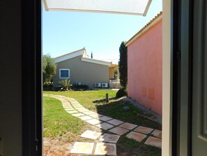 A view through a doorway into a courtyard with a paved path, a building with a tiled roof, and a wall with a window.